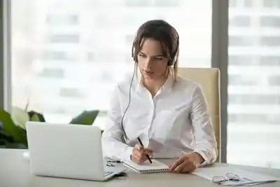 Woman with headphones listening to her computer and taking notes